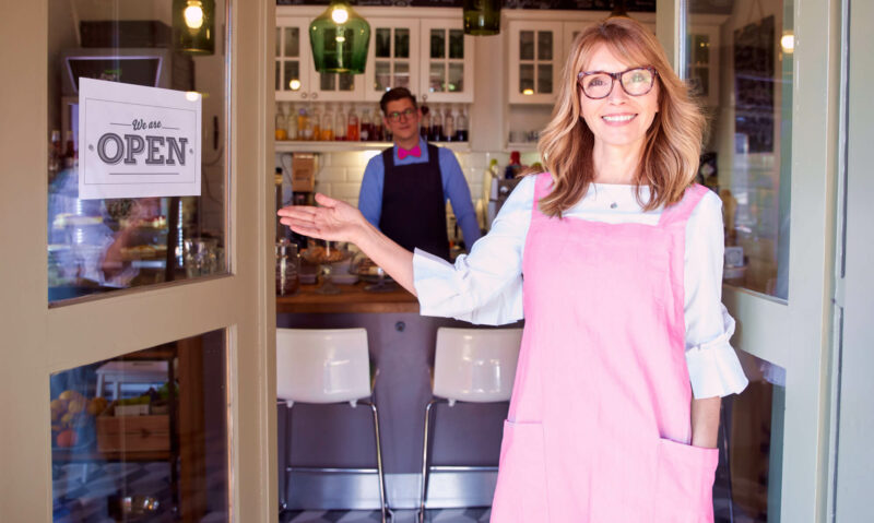 Shop owner in pink apron welcoming you into her store with open sign