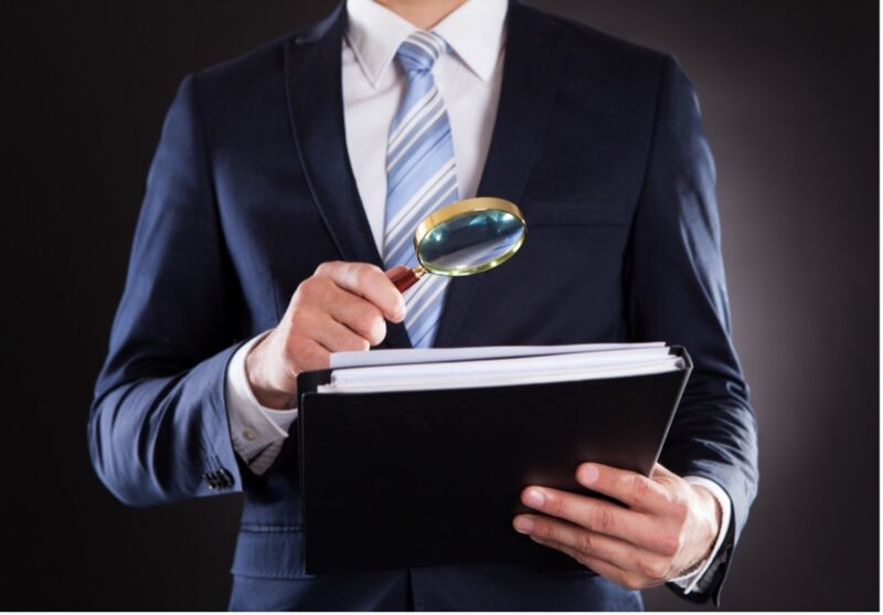 Man with a magnifying glass and looking at contract documents