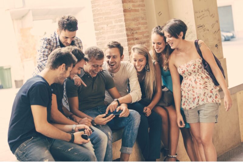 Young millennials hanging out and laughing together at something on a smartphone