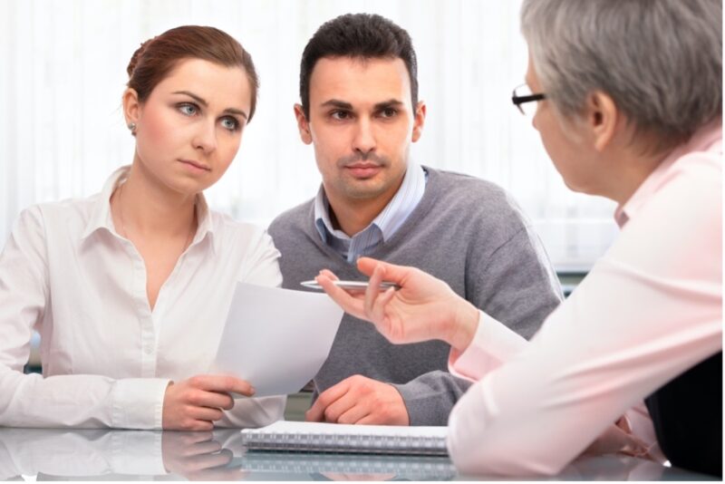 A man and woman in business casual attire discuss estate planning documents with an attorney in an office setting.