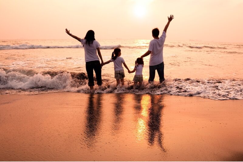 A family standing in surf at sunset.