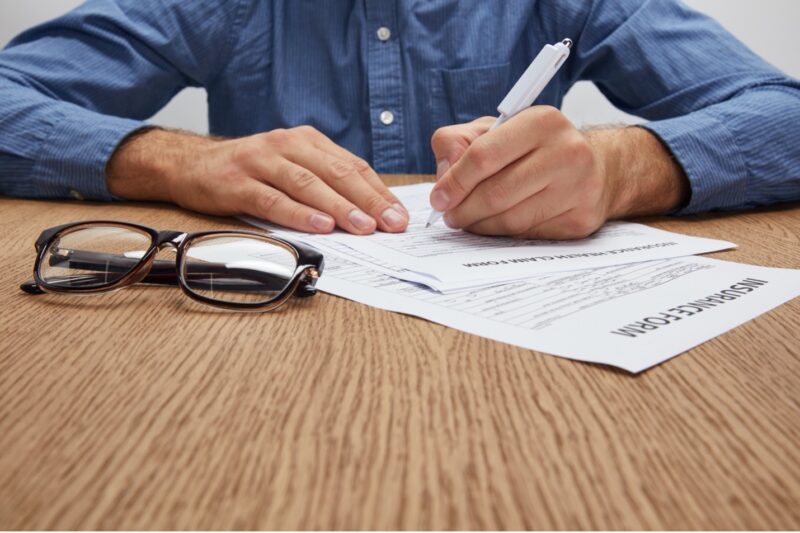A man filling out insurance claims forms at a laminate desk.