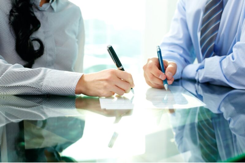 Two people in business attire, signing trust documents.